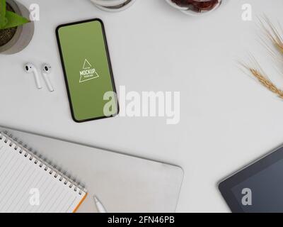 Vue de dessus du smartphone maquette sur la table de travail avec ordinateur portable, écouteurs et fournitures Banque D'Images