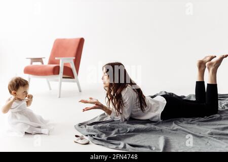 Mère ou baby sitter discutant avec une petite fille posée sur un sol chaud à la maison, maman concentrée aidant enfant fille à apprendre à dire de nouveaux mots ensemble Banque D'Images