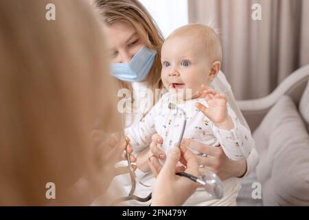 Femme médecin pédiatre examinant bébé fille souriante avec stéthoscope faire un mois de contrôle, vérifie le coeur et les poumons. La jeune mère blonde a poil dur Banque D'Images