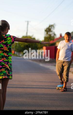 Recentrer les jeunes filles et garçons heureux jouant sur le skateboard dans la rue. Elle a mis les bras sur les côtés des enfants caucasiens de la circonscription de Penny board, pratiquant le skat Banque D'Images