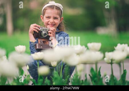 Petite fille avec l'ancien appareil photo vintage faisant des photos de tulipes dans le jardin fleuri Banque D'Images