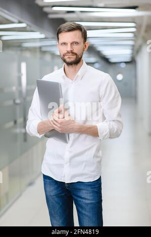 portrait d'un jeune homme dans une chemise blanche au bureau. Le directeur du bureau tient un ordinateur portable Banque D'Images