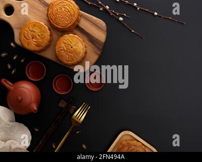 Vue de dessus d'une table moderne sombre avec plateau à thé, gâteaux de lune sur plateau en bois, fourchette, décoration et espace de photocopie. Le caractère chinois sur le gâteau de lune représente ' Banque D'Images