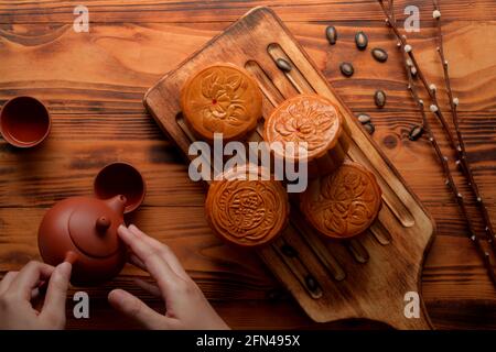 Les mains de femmes versant du thé chaud avec des gâteaux de lune traditionnels sur plateau en bois le caractère chinois sur le gâteau de lune représentent 'cinq grains et rôti de porc' dans Banque D'Images