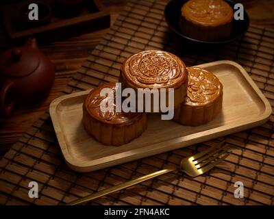 Vue rapprochée des gâteaux de lune traditionnels sur une assiette en bois avec fourchette et plateau à thé. Le caractère chinois sur le gâteau de lune représente 'cinq grains et rôti de por Banque D'Images