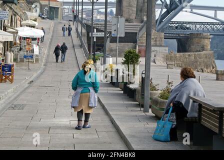 Les gens marchent dans une rue près du fleuve Douro. Une femme grasse se repose en regardant la route. La vie urbaine au Portugal. Banque D'Images