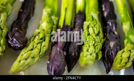 Une rangée d'asperges vertes et violettes saupoudrées de sel et d'huile d'olive préparée pour griller. Macro, mise au point différentielle. Banque D'Images