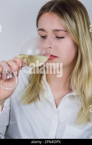 Portrait d'une belle jeune femme blonde qui renifle le vin blanc dans le verre pour sentir son bouquet à un vin dégustation Banque D'Images