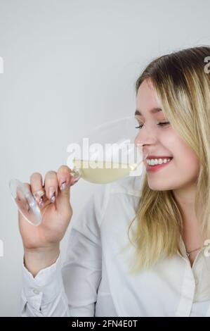 Portrait d'une belle jeune femme blonde qui renifle le vin blanc dans le verre pour sentir son bouquet à un vin dégustation Banque D'Images