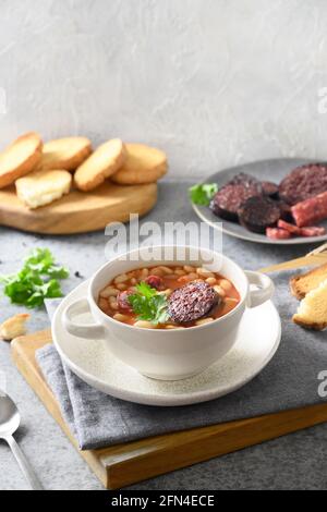 Fabada traditionnelle Asturiana avec haricot, saucisse de sang servi des toasts croustillants frais sur table grise. Orientation verticale. Cuisine espagnole. Banque D'Images