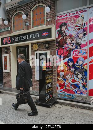 Un vieux homme d'affaires traverse les rues d'Akihabara Electric Town. Un homme âgé passe devant un faux pub japonais britannique, à côté d'un panneau d'affichage Banque D'Images