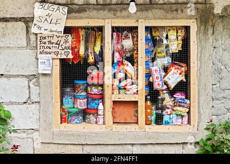 La fenêtre grillée fonctionne comme un magasin de quartier sari-sari aux Philippines. On vend des collations, des boissons gazeuses, des bonbons et des articles d'épicerie à un prix bon marché Banque D'Images