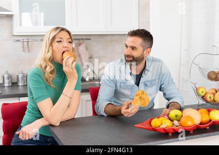 Un couple sucré mange des croissants pour le petit déjeuner. Les jeunes mariés mangent ensemble dans la cuisine. Bonheur, fruit et style de vie. Banque D'Images