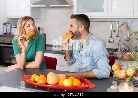 Un couple sucré mange des croissants pour le petit déjeuner. Les jeunes mariés mangent ensemble dans la cuisine. Bonheur, fruit et style de vie. Banque D'Images