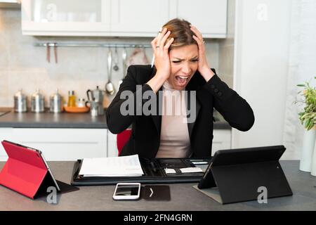 Une femme d'affaires surtravaillée et désespérée crie et crie dans la cuisine. La femme tient sa tête dans les mains comme elle souffre d'une panne nerveuse. Banque D'Images
