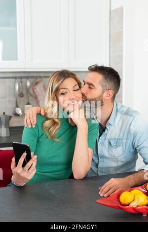 La femme blonde prend un selfie tout en étant embrassée par son petit ami. Une jeune fille avec une chemise verte se photographie pour les médias sociaux. Couple heureux. Banque D'Images