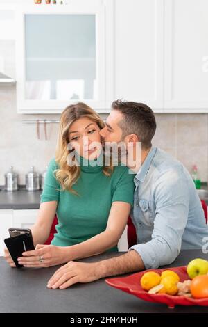 La femme blonde prend un selfie tout en étant embrassée par son petit ami. Une jeune fille avec une chemise verte se photographie pour les médias sociaux. Couple heureux. Banque D'Images