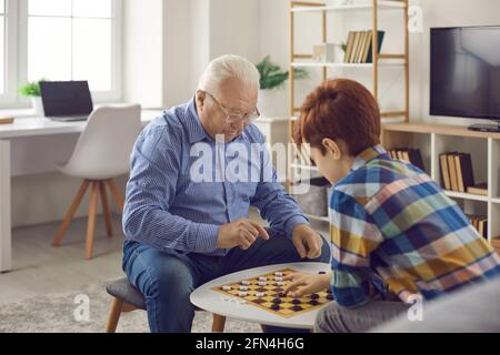 Senior homme concentrique grand-père assis et jouant des dames avec son petit-fils Banque D'Images