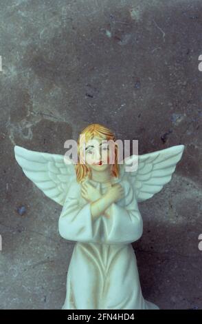 Modèle en porcelaine d'ange de fille en robe blanche avec cheveux rouges et bras croisés agenouillés devant le mur de marbre Banque D'Images