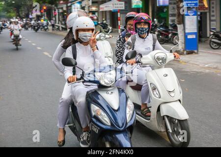 De jolies écolières vietnamiennes portant des robes blanches traditionnelles ao dai s'assoient sur des scooters donnant le signe de paix, Da Nang, Vietnam Banque D'Images