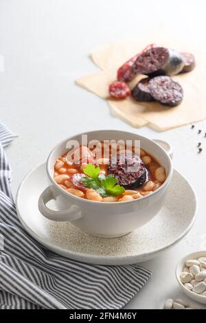 Asturiana fabada traditionnelle avec haricot, saucisse de sang sur table blanche. Orientation verticale. Cuisine espagnole. Gros plan. Banque D'Images