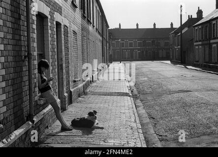 Une fille et son chien à l'extérieur de sa maison dans une rue où la plupart des maisons sont braquées en attendant la démolition, Splott, Cardiff, 1975 Banque D'Images