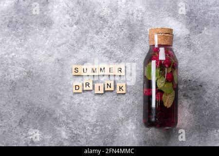 Limonade de cassis à la menthe framboise en bouteille de verre et lettres en bois écrites mot Summer Drink. Concept de boisson saine, eau infusée sur contr. Gris Banque D'Images