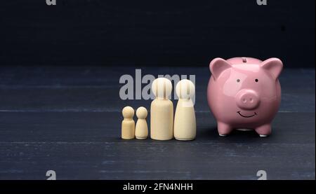 figurines de famille en bois et banque de porc en céramique rose, concept d'épargne, contrôle du budget. Planification à long terme de la distribution des fonds pour les achats importants Banque D'Images