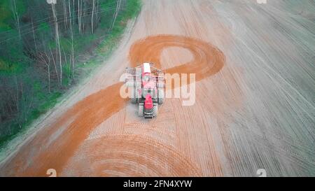 Le tracteur rouge effectue un demi-tour dans le champ et plère, cultive le champ le jour du printemps. Photo avec un drone Banque D'Images