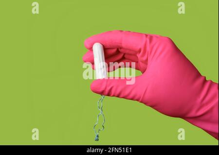 Personne méconnaissable avec un gant rose tenant un tampon de coton sur fond vert. Banque D'Images