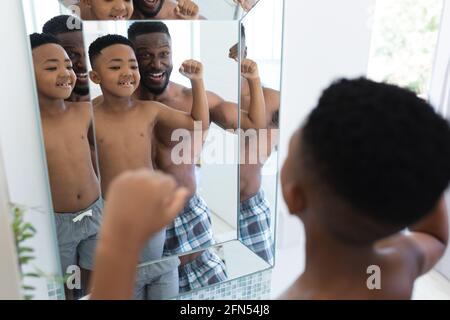 Père et fils afro-américains dans la salle de bains, regardant dans le miroir montrant des muscles Banque D'Images