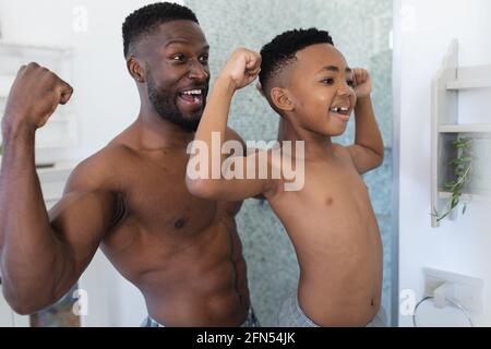 Père et fils afro-américains dans la salle de bains, regardant dans le miroir montrant des muscles Banque D'Images