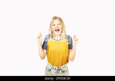 Jeune fille adolescente à l'indécise avec des cheveux blonds vêtue d'un t-shirt de baseball jaune avec des manches bleues, debout dans une posture gagnante avec les poings vers le haut et la Banque D'Images