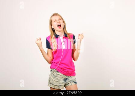 Jeune adolescente naturelle femme blonde souriante dansant, chantant le long de sa chanson préférée avec des écouteurs. Arrière-plan blanc, espace de copie. Belle femme Banque D'Images