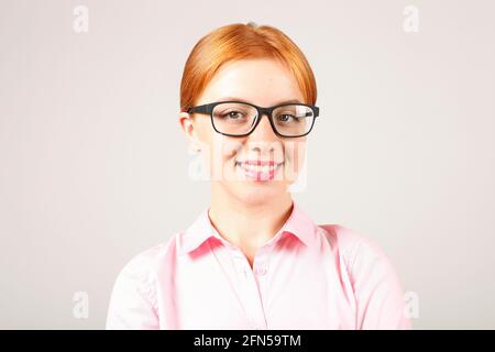 Gros plan de la belle jeune femme d'affaires avec des cheveux rouges naturels portant des lunettes noires et un chemisier rose, tenue formelle stricte robe cabillaud Banque D'Images