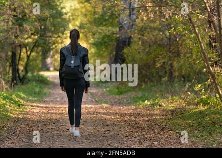 Jeune fille marchant dans un parc déserté. Marchez seul avec vous-même. Vue arrière. Banque D'Images