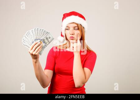 L'argent comme un cadeau de Noël concept. Portrait d'une jeune femme heureuse à tête rouge tenant un bouquet de cent billets de dollars reçus comme cadeau du nouvel an. GR Banque D'Images
