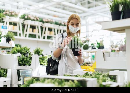 Jeune femme en masque de protection achetant des fleurs dans un centre de jardin. Banque D'Images