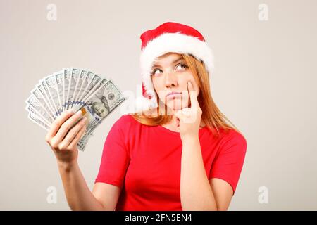 L'argent comme un cadeau de Noël concept. Portrait d'une jeune femme heureuse à tête rouge tenant un bouquet de cent billets de dollars reçus comme cadeau du nouvel an. GR Banque D'Images