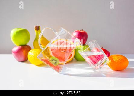 Verser l'eau du pichet dans le verre, beaucoup de fruits mûrs colorés sur le fond. Banque D'Images