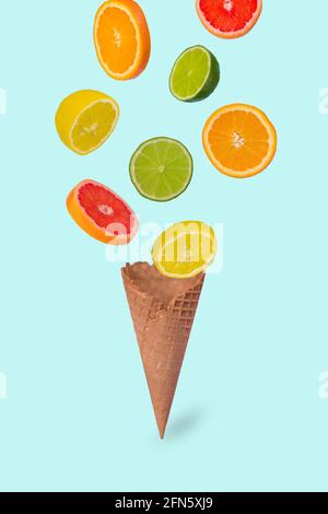 Idée minimale avec un cône de crème glacée et des tranches d'orange, de citron vert, de citron et de pamplemousse frais, sur fond bleu pastel. Concept minimal de fruits d'été.vitamines Banque D'Images