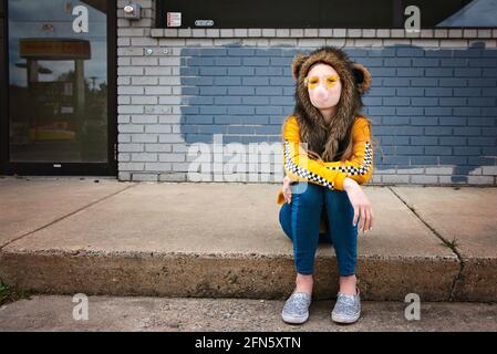 Tween fille assise sur le trottoir avec des lunettes de soleil et une cagoule. Banque D'Images