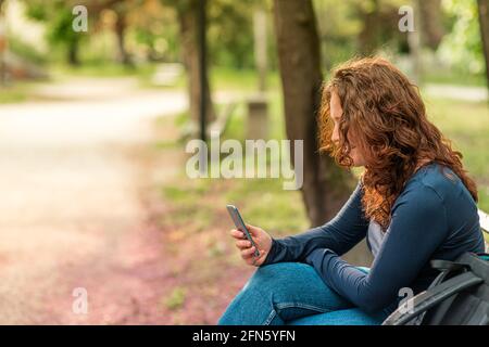 Portrait de charmante jeune femme aux cheveux rouges avec smartphone un parc Banque D'Images