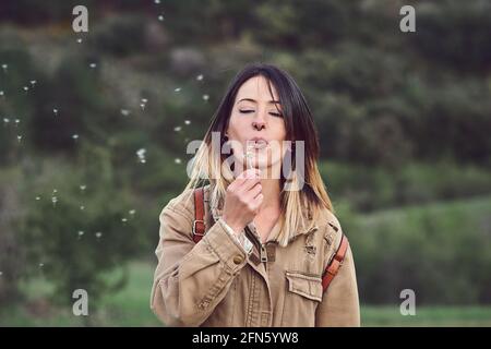 Femme soufflant un pissenlit.elle est sur la montagne. Banque D'Images