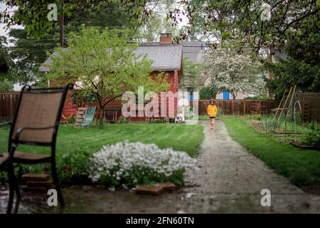 Un petit enfant marche sur le chemin sous la pluie dans l'arrière-cour jardin Banque D'Images