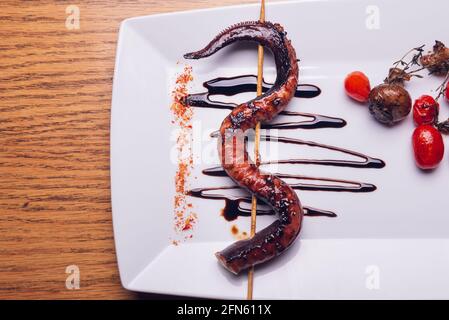 Pieuvre grillée sur une assiette blanche avec tomates cerises et champignons Banque D'Images
