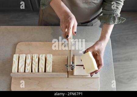Une femme fait du savon naturel fait main.le savon fini est coupé en morceaux à l'aide d'une machine spéciale. Spa à la maison. Petite entreprise. Banque D'Images