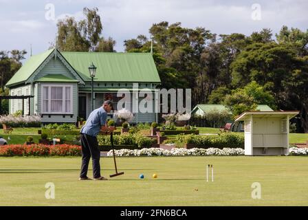 Un croquet-joueur conduisant le ballon à travers un panier sur la pelouse des jardins du Gouvernement de Rotorua. Banque D'Images