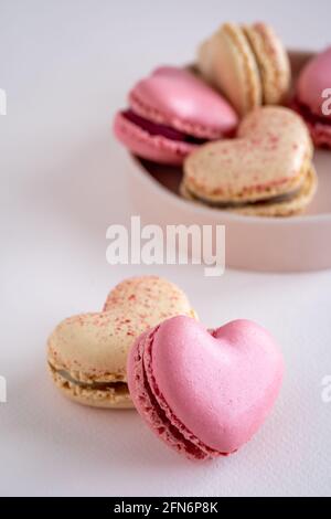 Un groupe de biscuits de macaron français en forme de coeur sur une assiette ronde et deux à l'avant, saveur de vanille et de fraise, verticale, espace de copie Banque D'Images