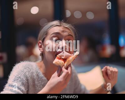 Une jeune femme mange une pizza du service de livraison au bureau Banque D'Images